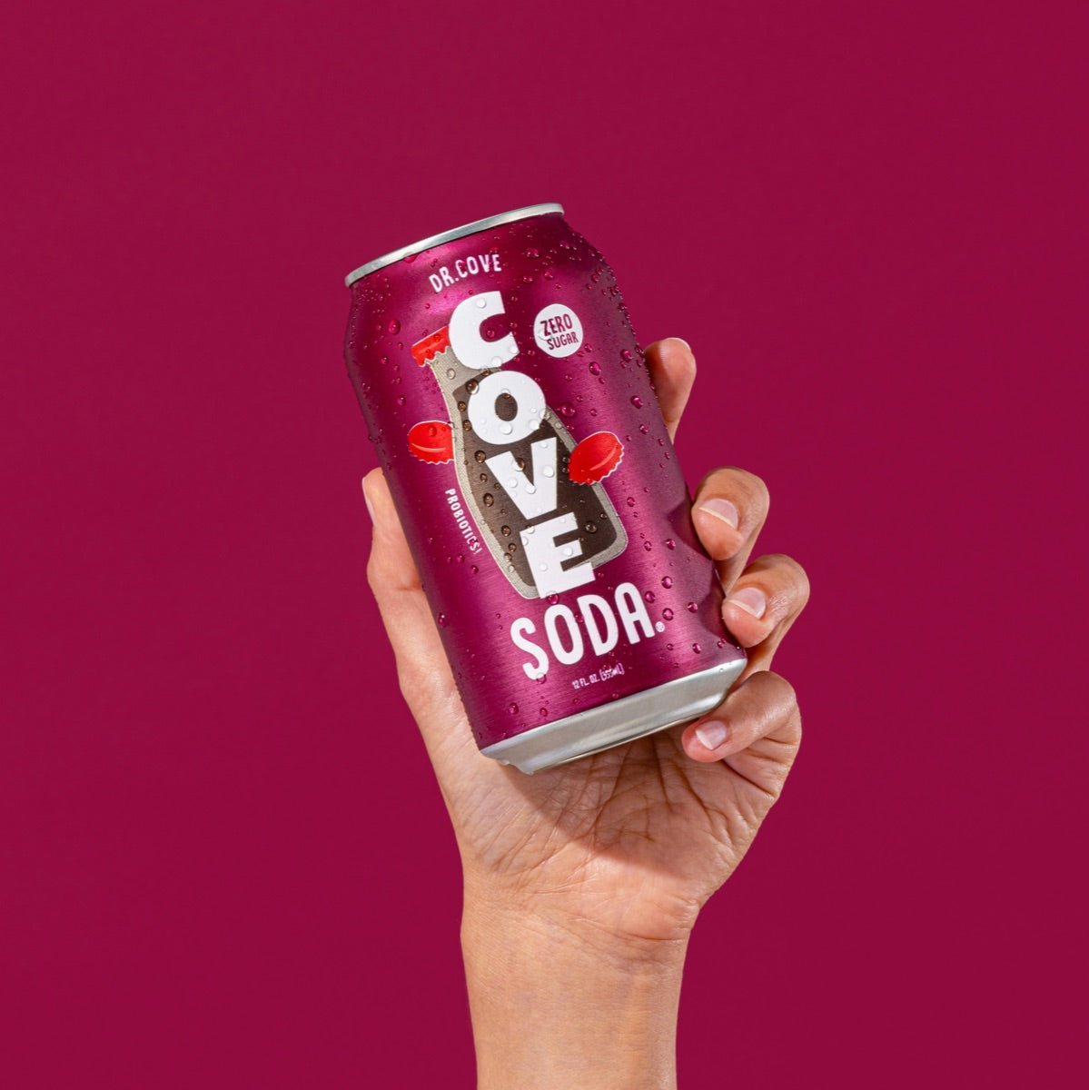 Hand holding a frosted Dr. Cove zero-sugar soda can against a deep berry backdrop