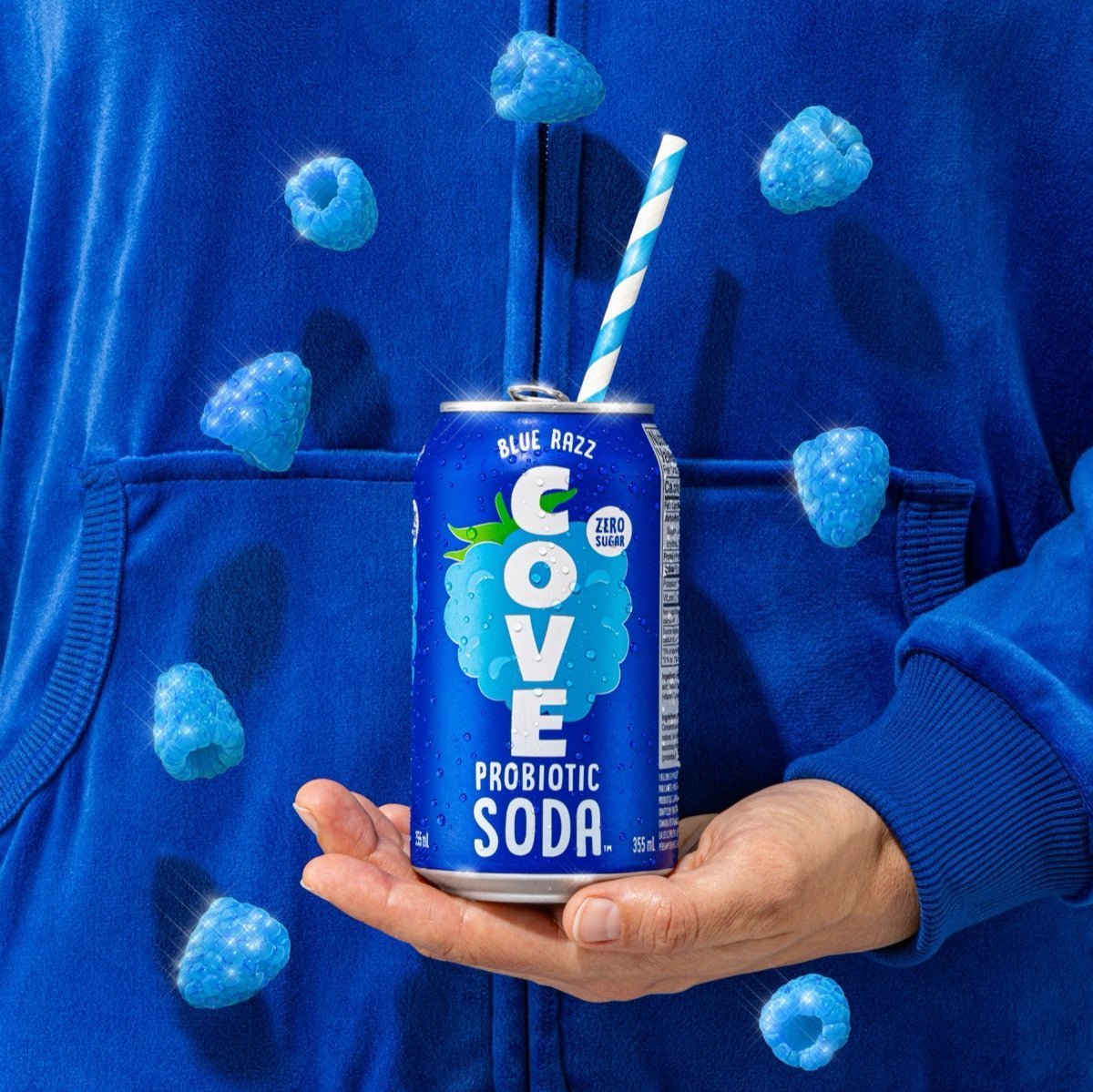Hand holding a Cove Blue Razz can with a paper straw and floating blue raspberries