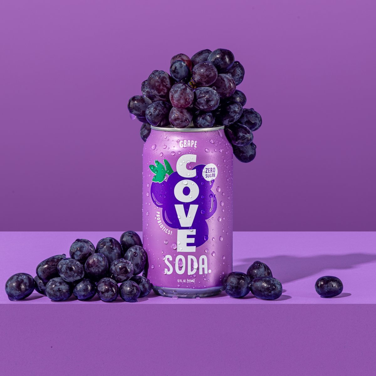 A Cove Grape can surrounded by purple grapes on a violet backdrop